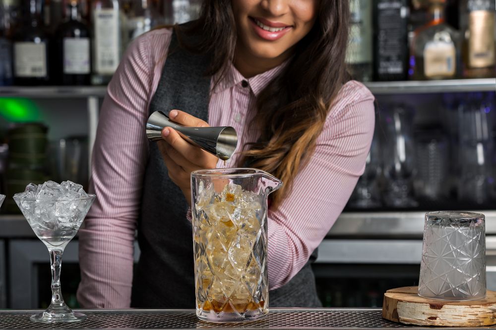 Smiling bartender pouring spirits to a stirring glass