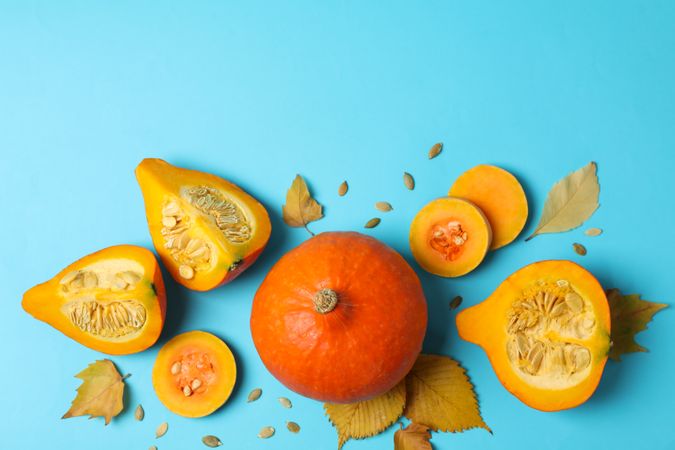 Composition with pumpkin, slices, leaves and seeds on blue background