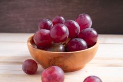 A bowl of red grapes sits on a wooden table