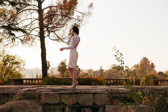 Side view full length photo of woman standing on stone wall looking away