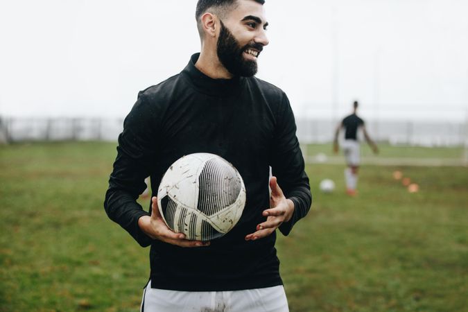 Smiling footballer standing on field holding a football during practice