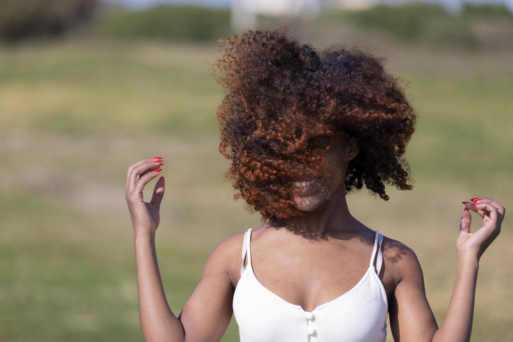 Female pictured outside in park with curly hair covering her face