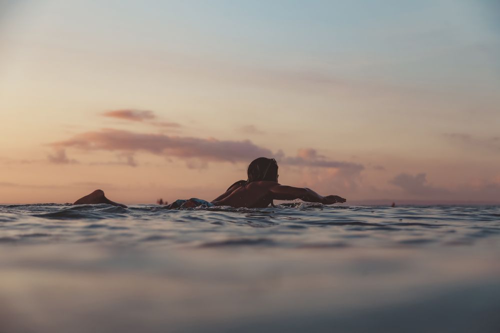 Man on surf board on waving water at sunset