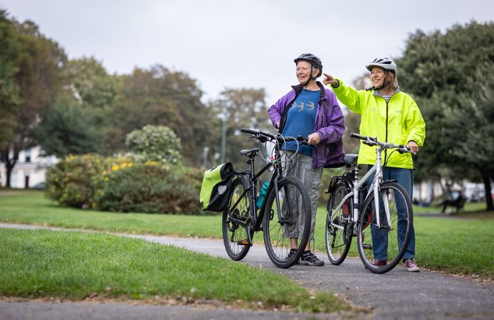 Two older people standing with bikes and looking in the distance