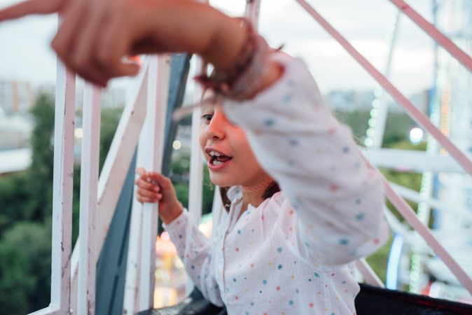 Cheerful girl riding Ferris wheel with parent