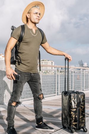 Portrait of a traveller man holding a smartphone and a carrying suitcase