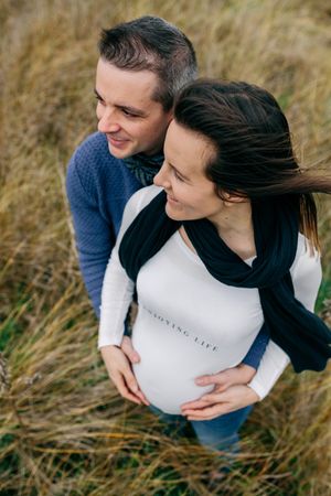 Pregnant person with partner hugging and holding belly