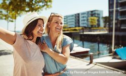 Two women laughing together and holding each other on sunny day next to the river 4dNZd0