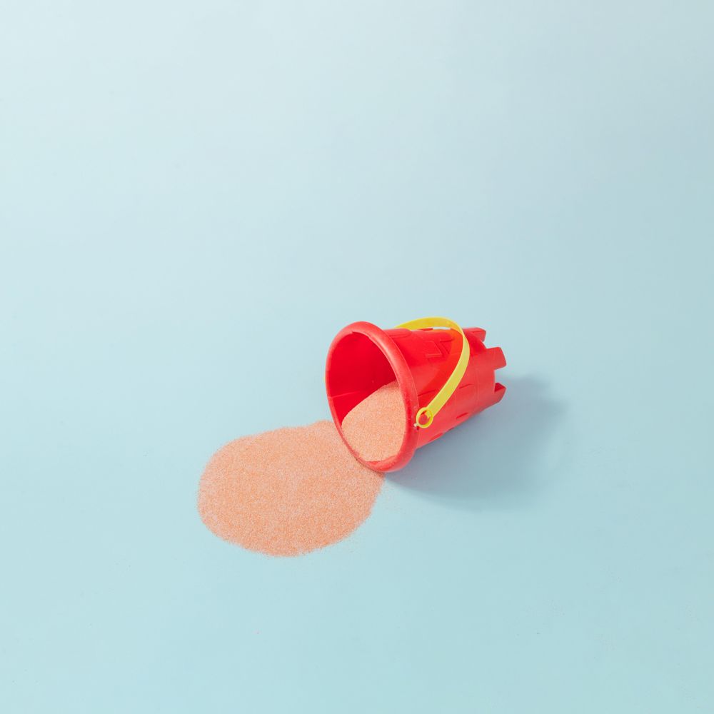 Sand castle bucket with spilled sand against pastel blue background