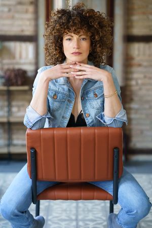Woman with curly hair sitting on chair reversed resting chin on hands