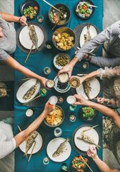 Group of people toasting drinks at table with whole fish on each plate and vegetable side dishes