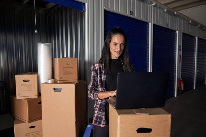 Focused woman browsing laptop near packed boxes