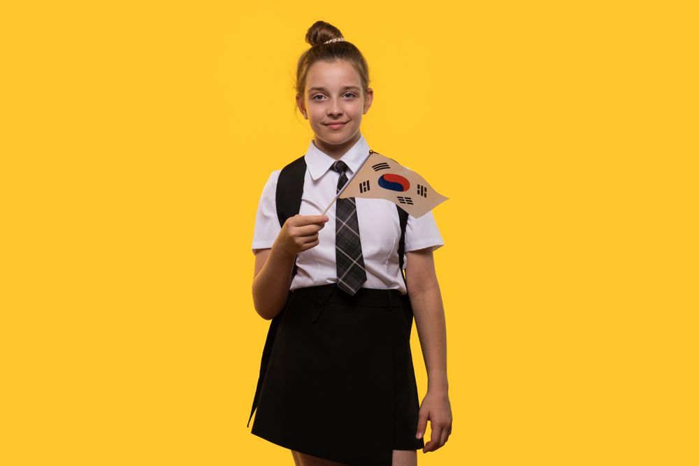 Schoolgirl holds South Korean flag while smiling confidently.