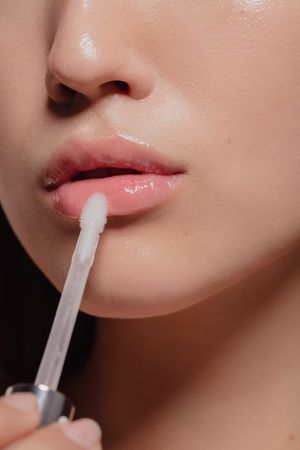 Cropped shot of woman applying lip glass to her lips