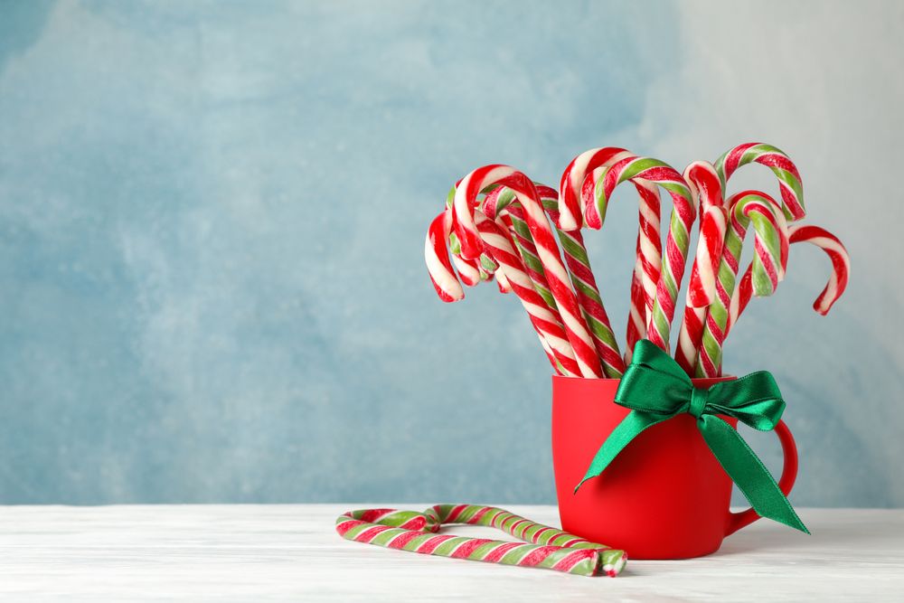 Candy canes in red cup on blue wooden background, space for text