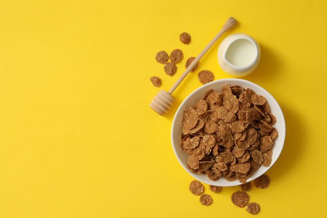 Milk and bowl of muesli on yellow background, top view