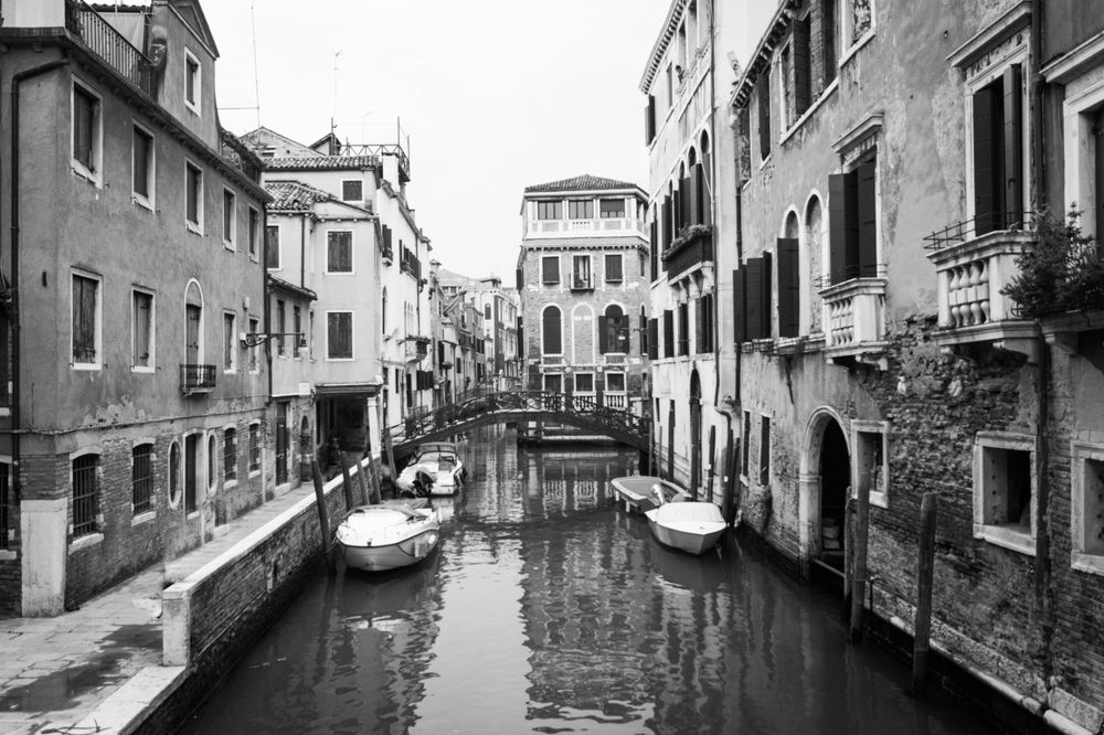 Grayscale photo of boat in water canal between buildings