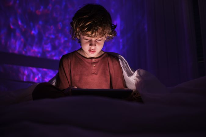 Calm boy watching video on tablet in darkness