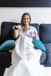 Happy woman sitting on a couch at home watching tv
