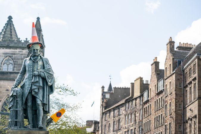 Aged monument with road cone on head