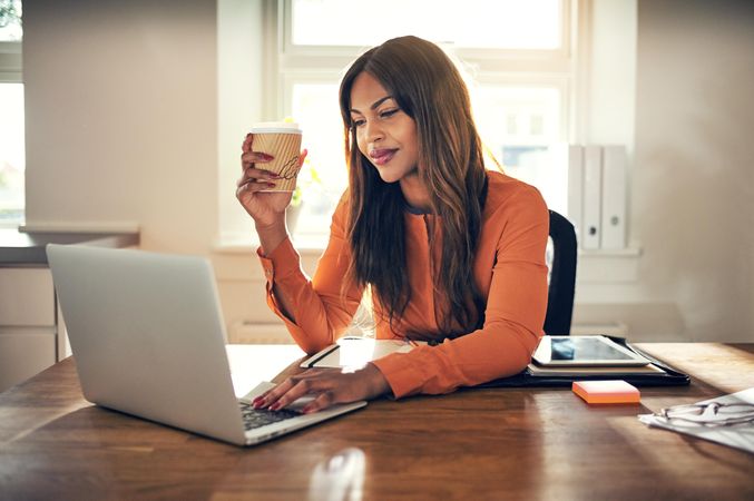 Businesswoman working on laptop with to go coffee in hand