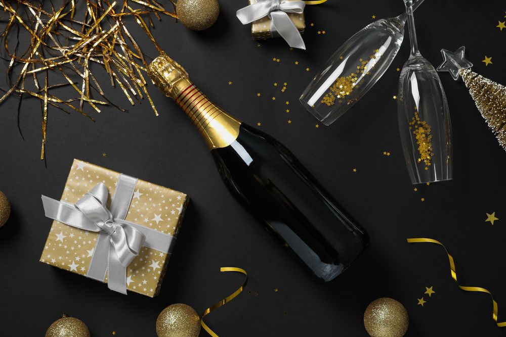 Champagne bottle, glasses and christmas baubles on dark background, top view