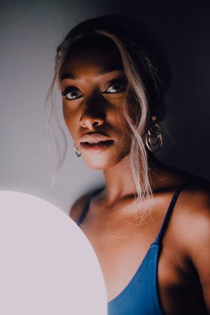 Black adult woman with illuminated balloon in darkness looking at camera