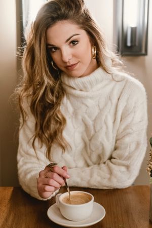 Elegant woman mixing coffee in cafe