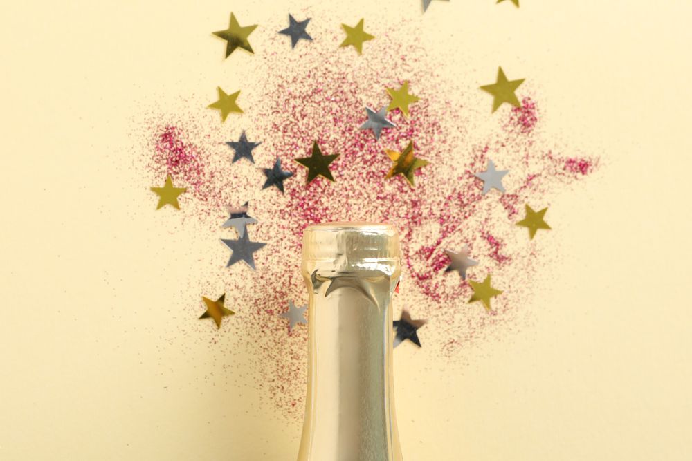 Champagne bottle and glitter on beige background, close up