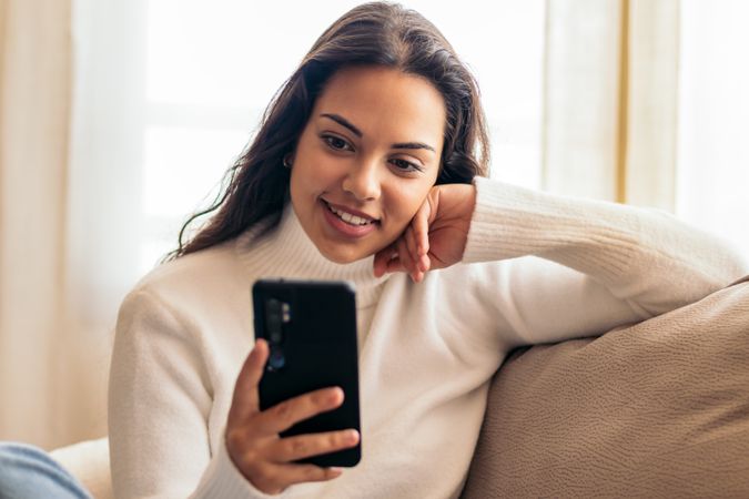 Connected at Home: Young Woman Sitting on Sofa Using Smartphone