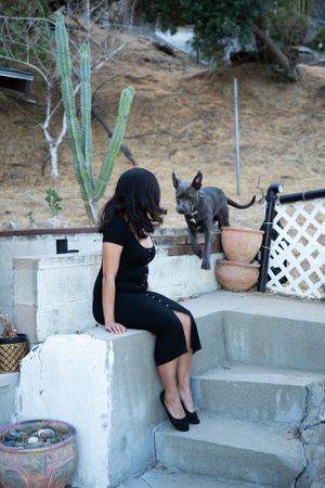 Woman sitting on cement steps in her yard with her dog running to greet her