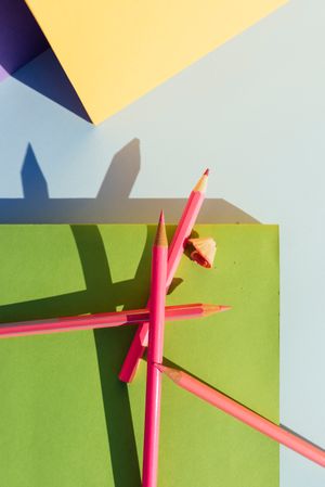 Pink pencils on green book, in space of geometric shapes.