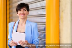 Smiling woman in blue blazer standing outside of shutter with digital tablet 4ZenqO