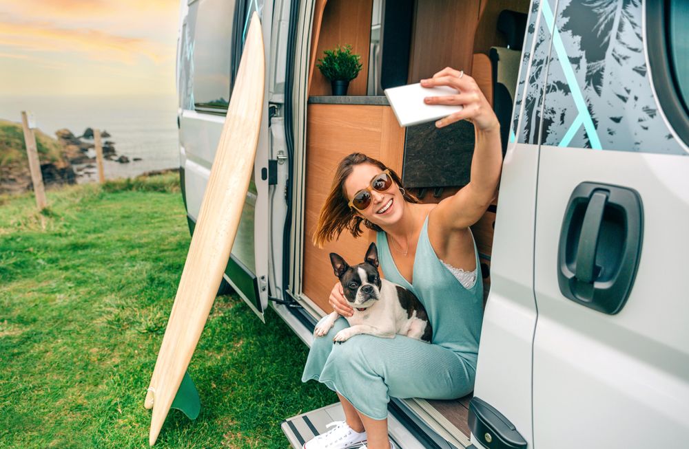 Smiling female sitting stoop of motorhome taking selfie with cute dog