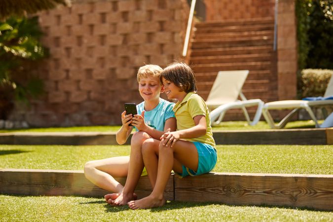 Cheerful boys browsing smartphone sitting on garden