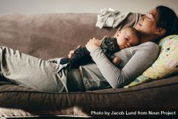 Side view of a woman lying on couch with eyes closed and holding her baby on her chest 0yxxRb