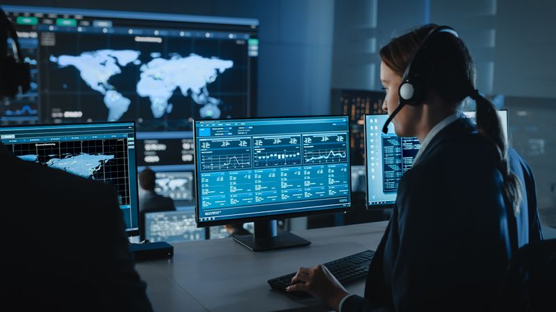 Analyst Monitors Global Data on Multiple Screens in Dark Control Room.
