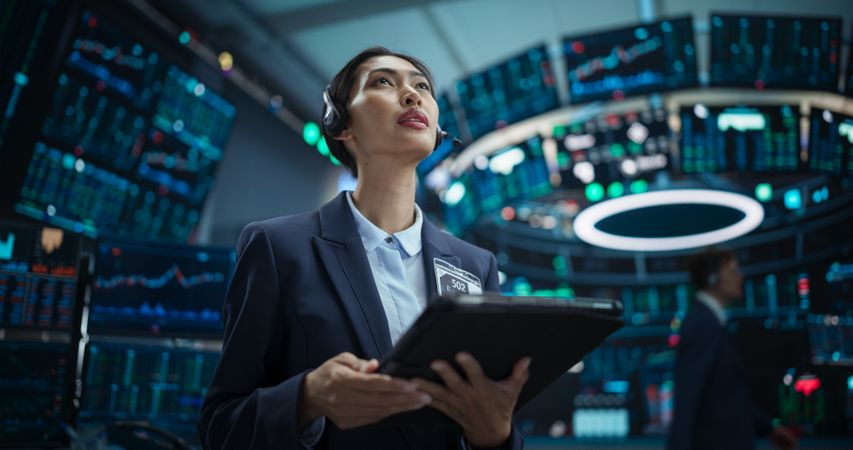 Young Female Stock Exchange Broker Working on Tablet Computer with Real-Time Stocks, Commodities and Exchange Market Charts. Professional Asian Investment Agent in Modern Office Building.
