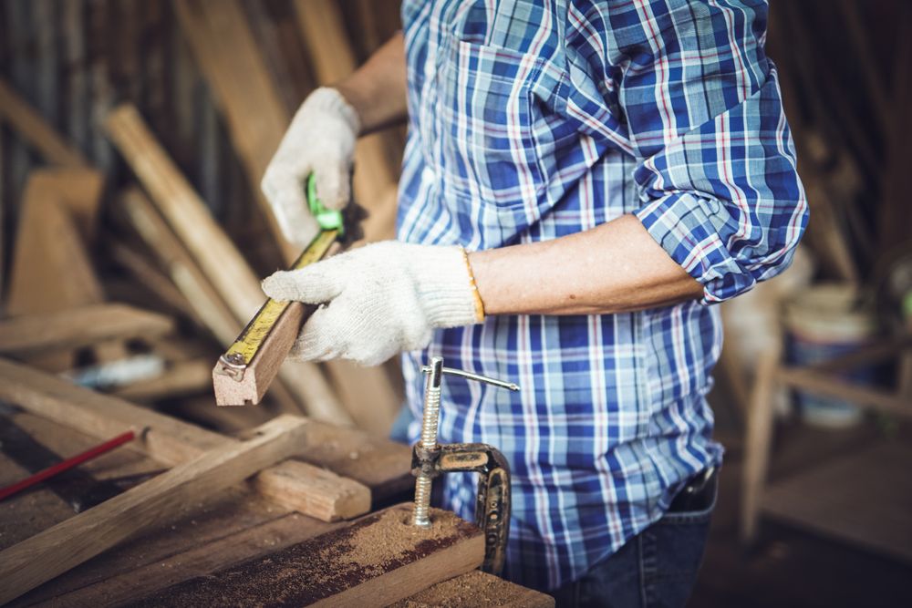 Hands of carpenter measuring a wooden panel in workshop for making furniture