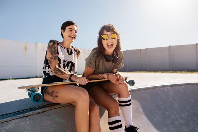 Two young women sitting on ramp at skate park laughing and having fun