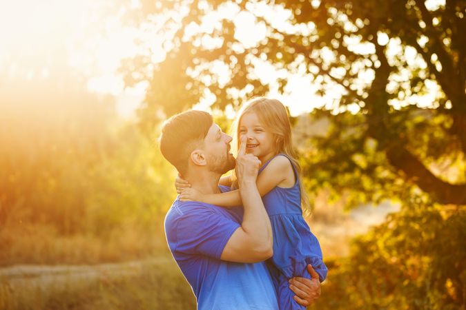 Man holding daughter  in sunny meadow smiling