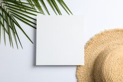 Square with space for text, palm leaves and straw hat on plain background, top view
