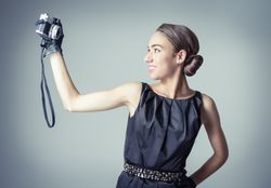 Smiling model in vintage clothing and gloves taking selfie with camera