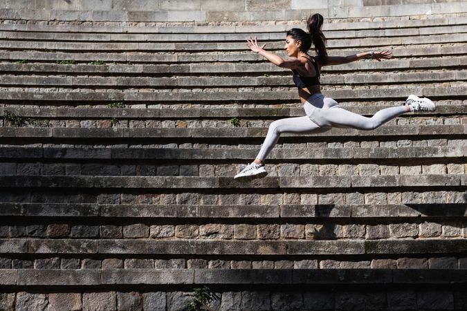 Flexible woman jumping above stone stairs