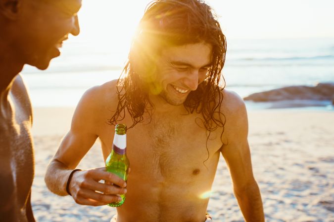 Smiling young man having beer with friend at beach