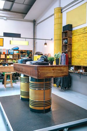 Wooden counter supported by fuel barrels with clothes stacks in a empty second hand apparel store