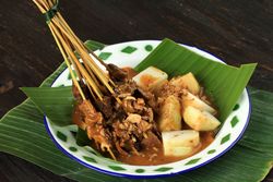 Bowl of beef sate skewers in spicy peanut sauce served on banana leaf