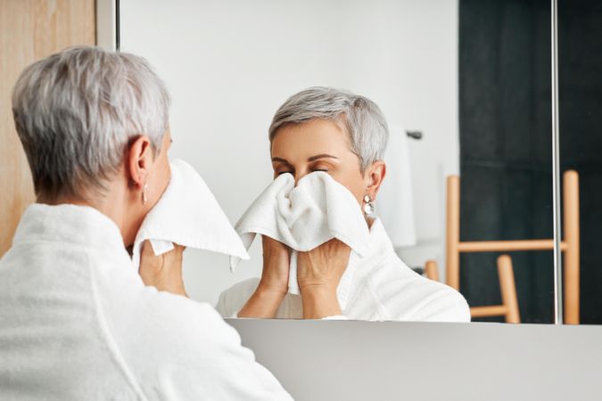 Older woman cleaning her face in bathroom mirror