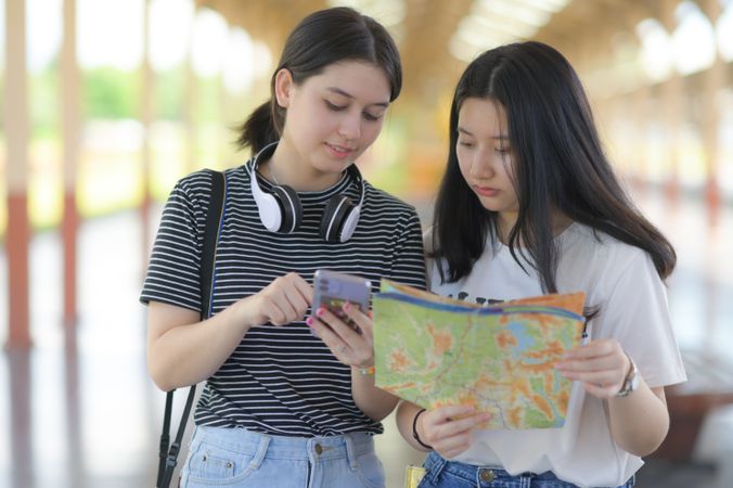 Two women holding smart phones and maps to travel