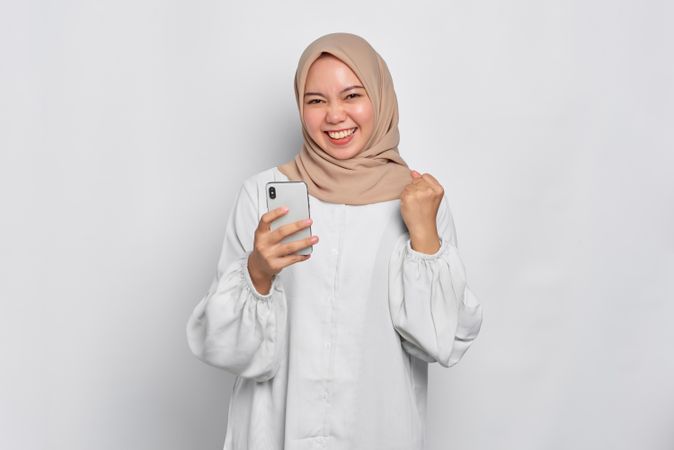 Asian female in headscarf receiving news she won on her cell phone